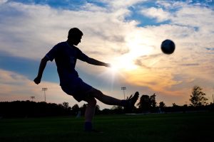 Silhuet af en fodboldspiller der sparker til en bold ved solnedgang