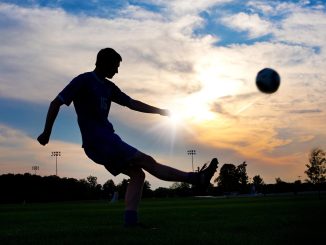 Silhuet af en fodboldspiller der sparker til en bold ved solnedgang